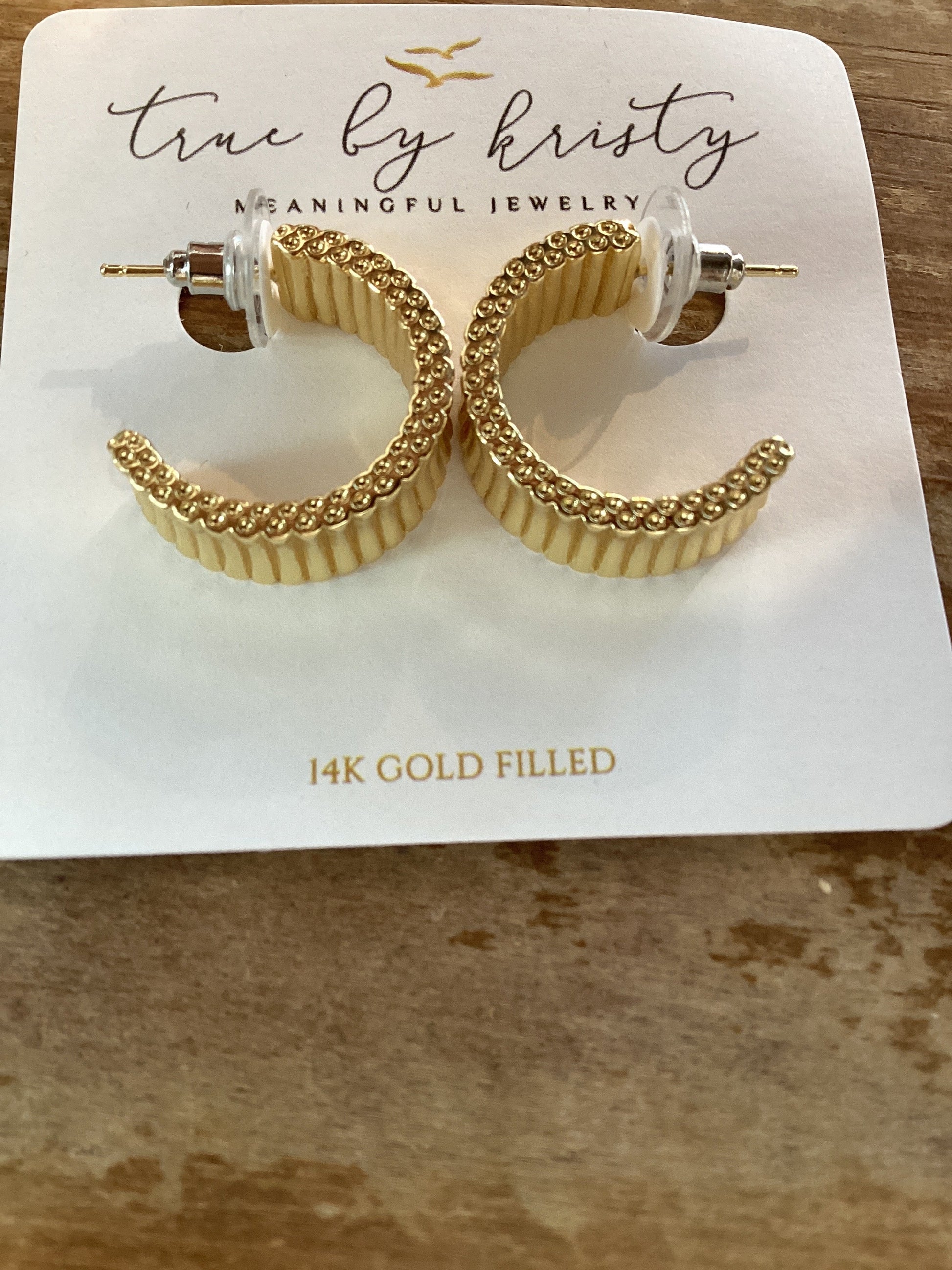 A pair of gold-filled crescent-shaped hoop earrings with a textured, ridged outer surface and a gold chain link inner band, displayed on a white card labeled 'true by kristy'.